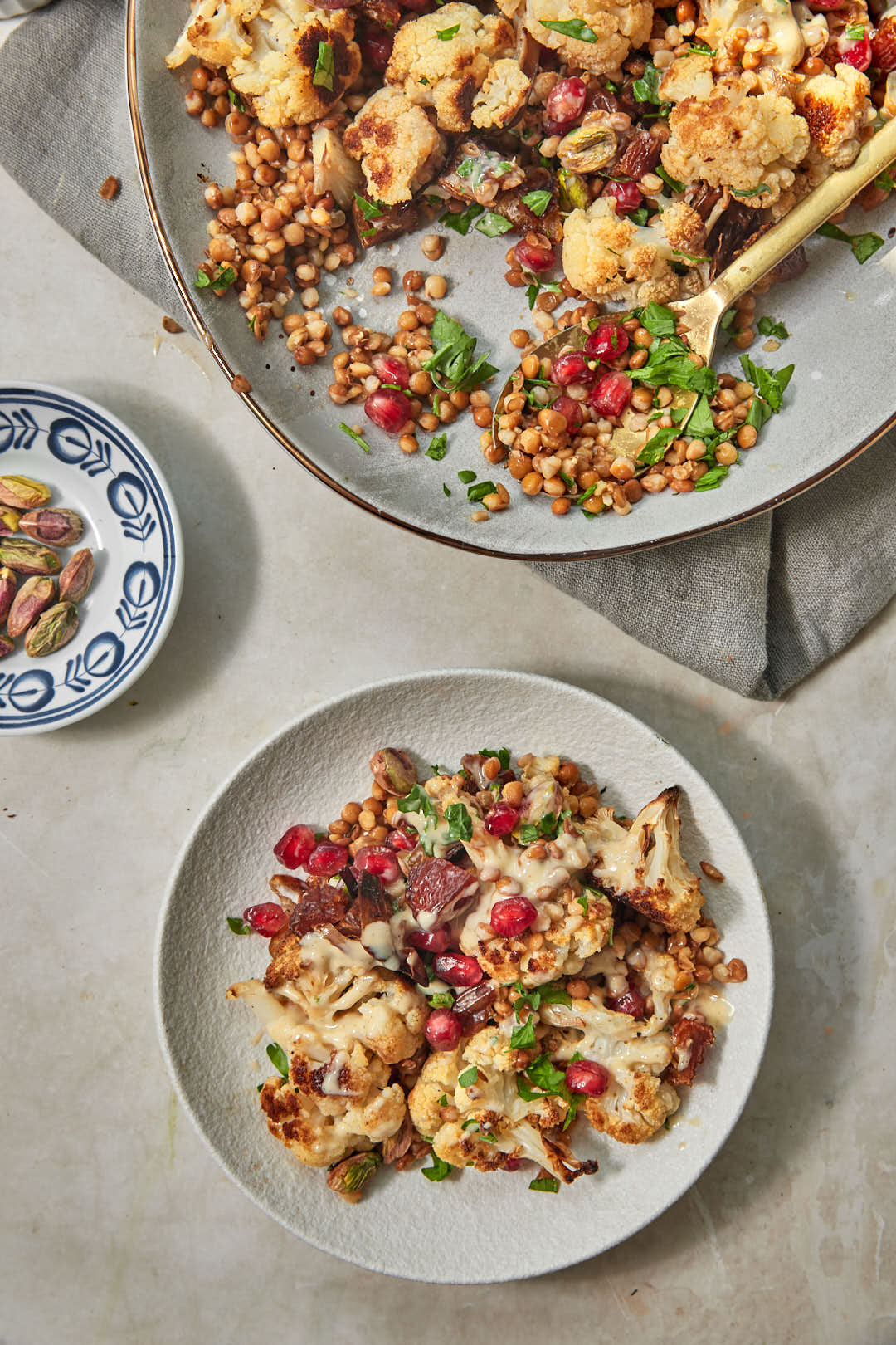 A plate of cauliflower lentil salad with the larger serving plate in the background with a wooden spoon taking a portion out.