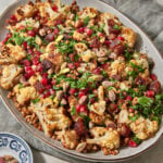 a large serving platter with roasted cauliflowers, lentils, pomegranate seeds, dates, and parsley.