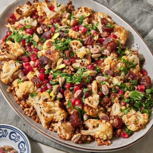 a large serving platter with roasted cauliflowers, lentils, pomegranate seeds, dates, and parsley.