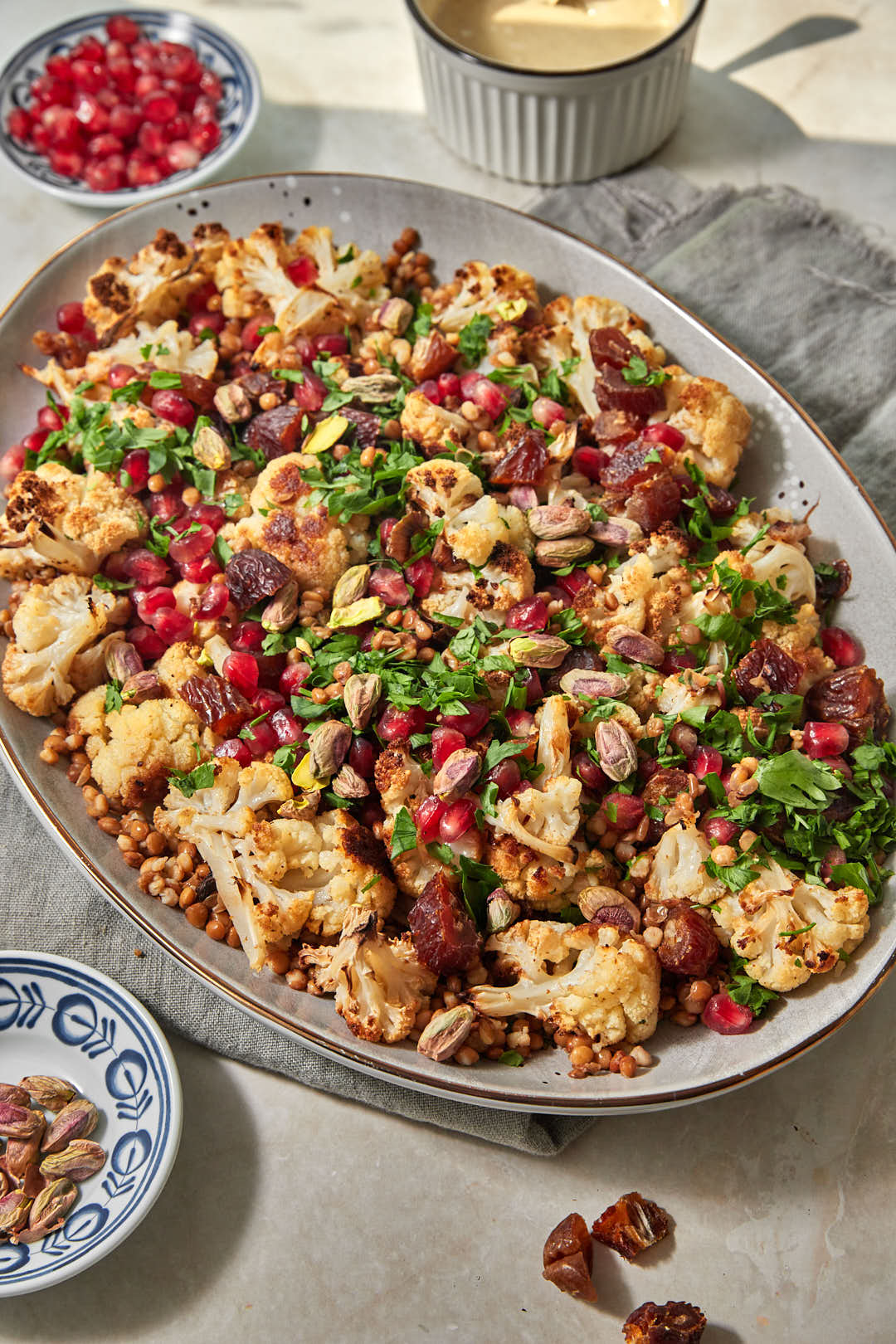 a large serving platter with roasted cauliflowers, lentils, pomegranate seeds, dates, and parsley.