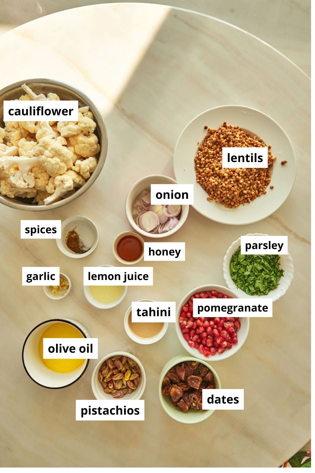 ingredients needed to make a cauiflower and lentil salad on a white marble background.