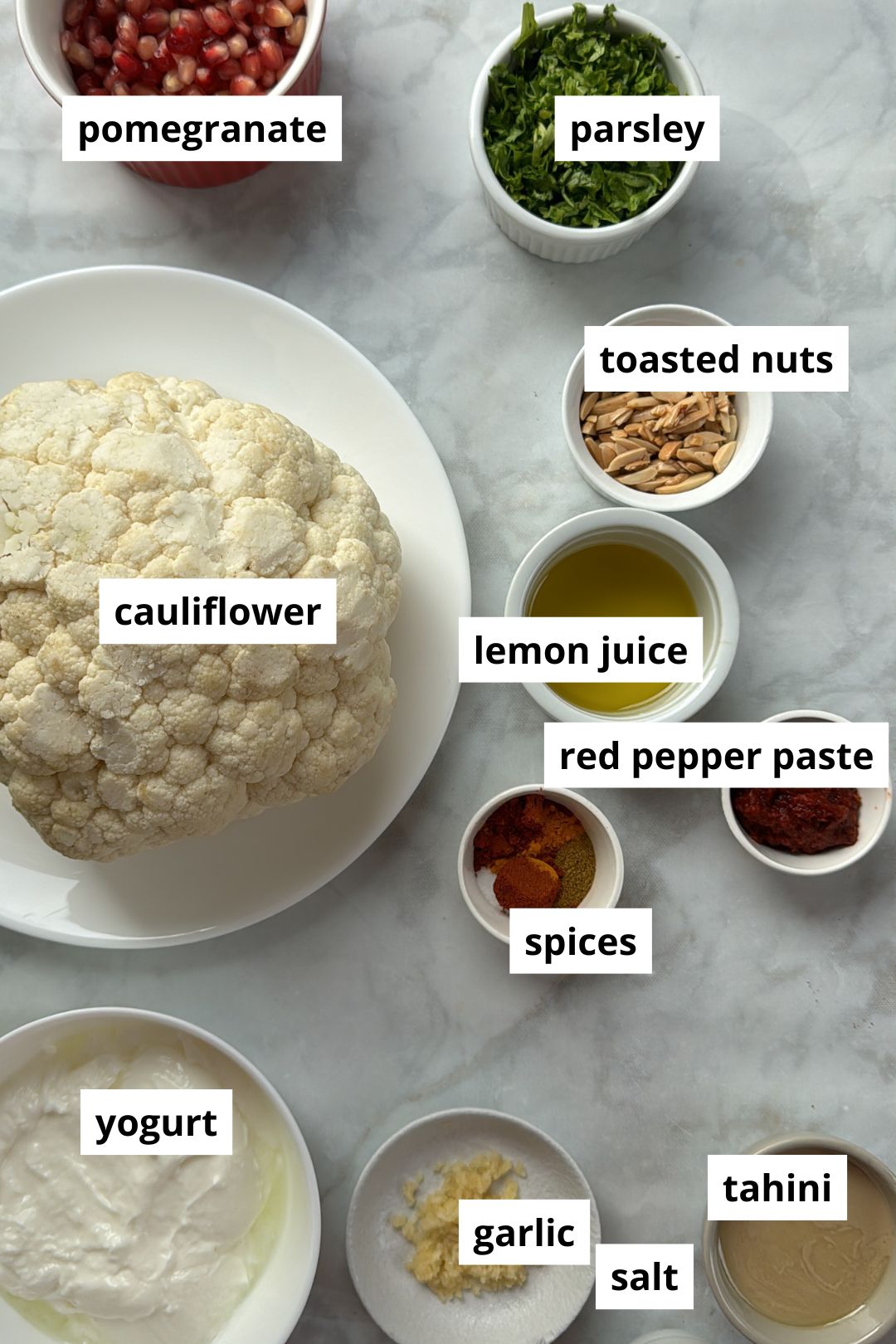 ingredients needed to make whole roasted cauliflower on a white marble background.