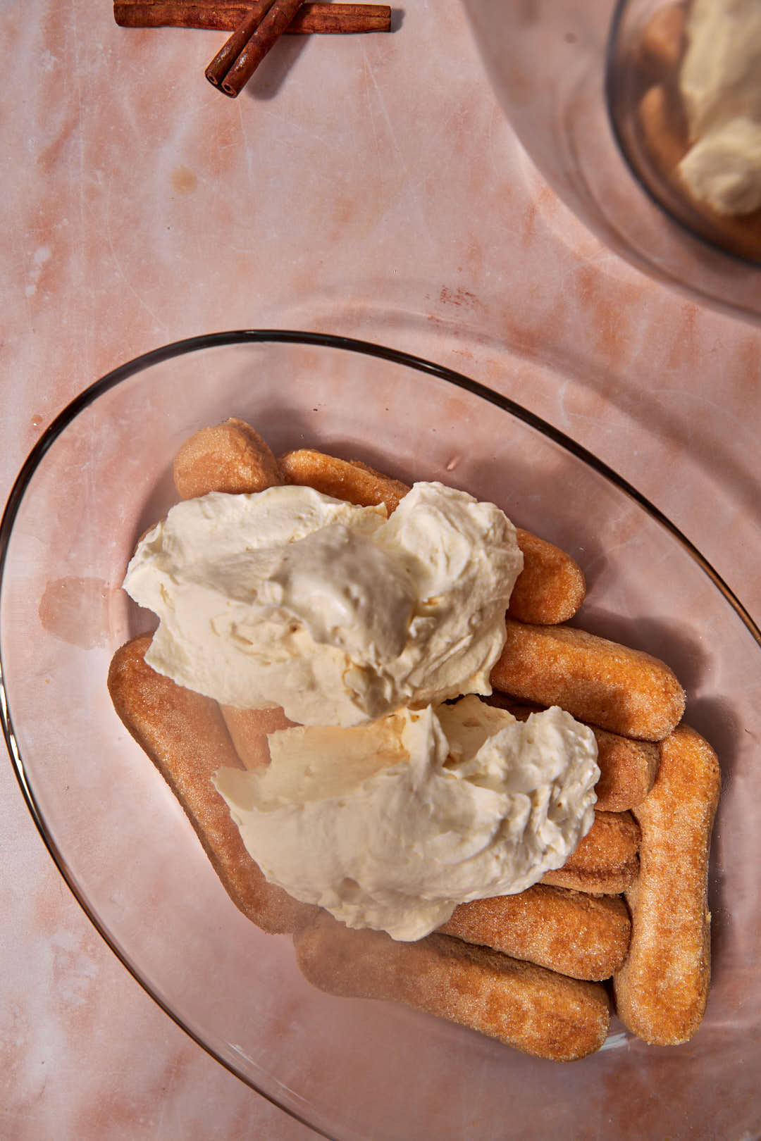 chai tiramisu cream being placed on ladyfingers in a pyrex dish.