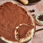 chai tiramisu being scooped out of a pyrex dish with a large spoon.
