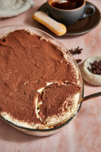 chai tiramisu being scooped out of a pyrex dish with a large spoon.