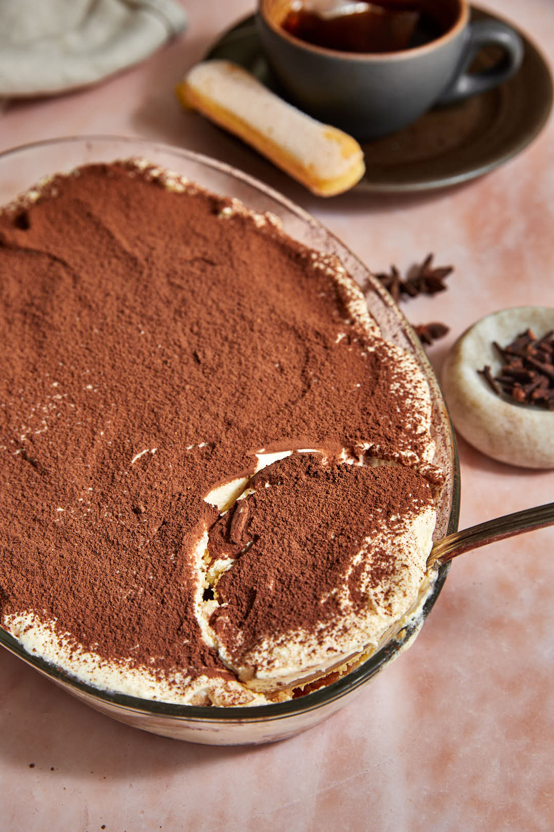 chai tiramisu being scooped out of a pyrex dish with a large spoon.