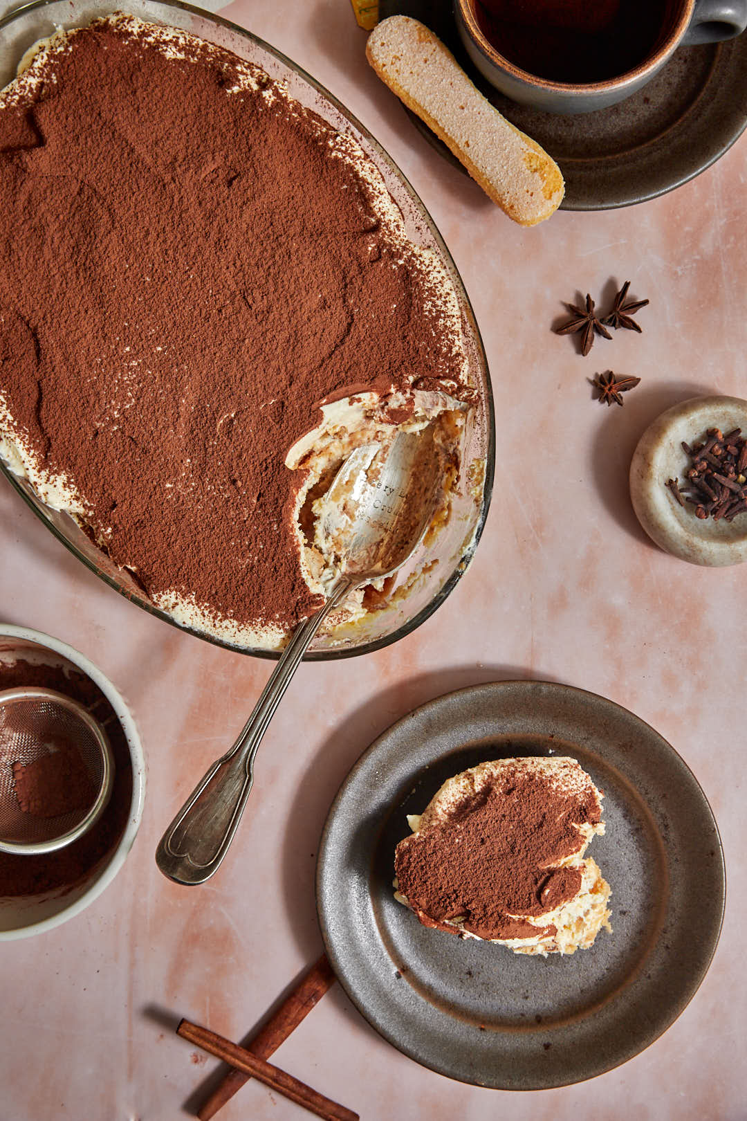 photo of tiramisu with a scoop on a plate and star anise pods and a cup of tea in the background.