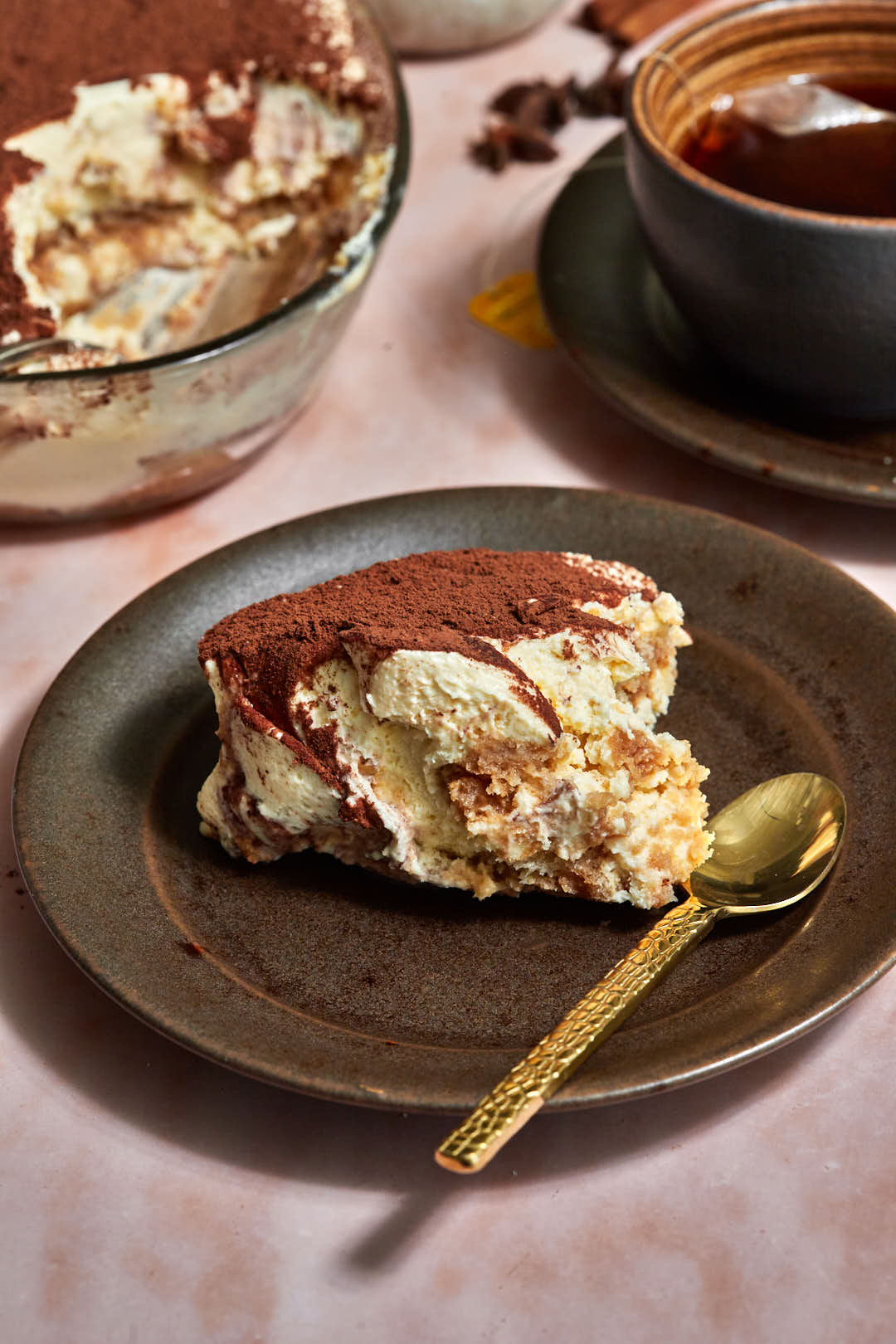 scoop of chai tiramisu on a dark brown plate with a gold spoon.