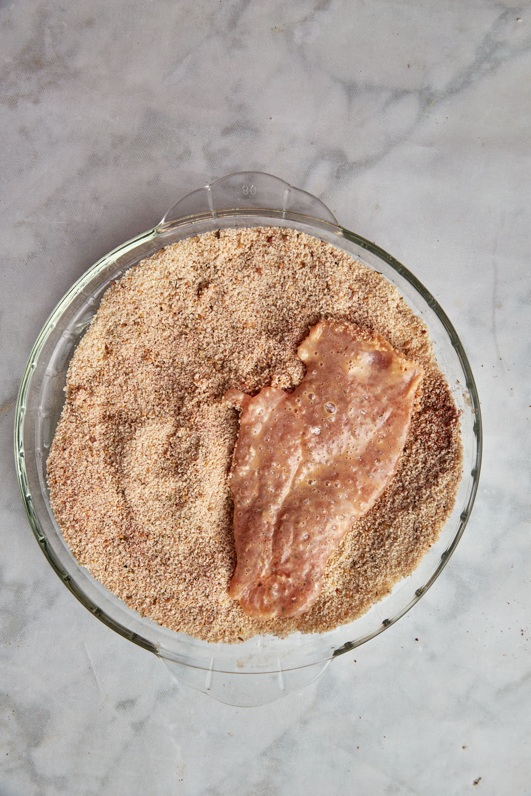 chicken breast dredged in bread crumbs in a pie plate.