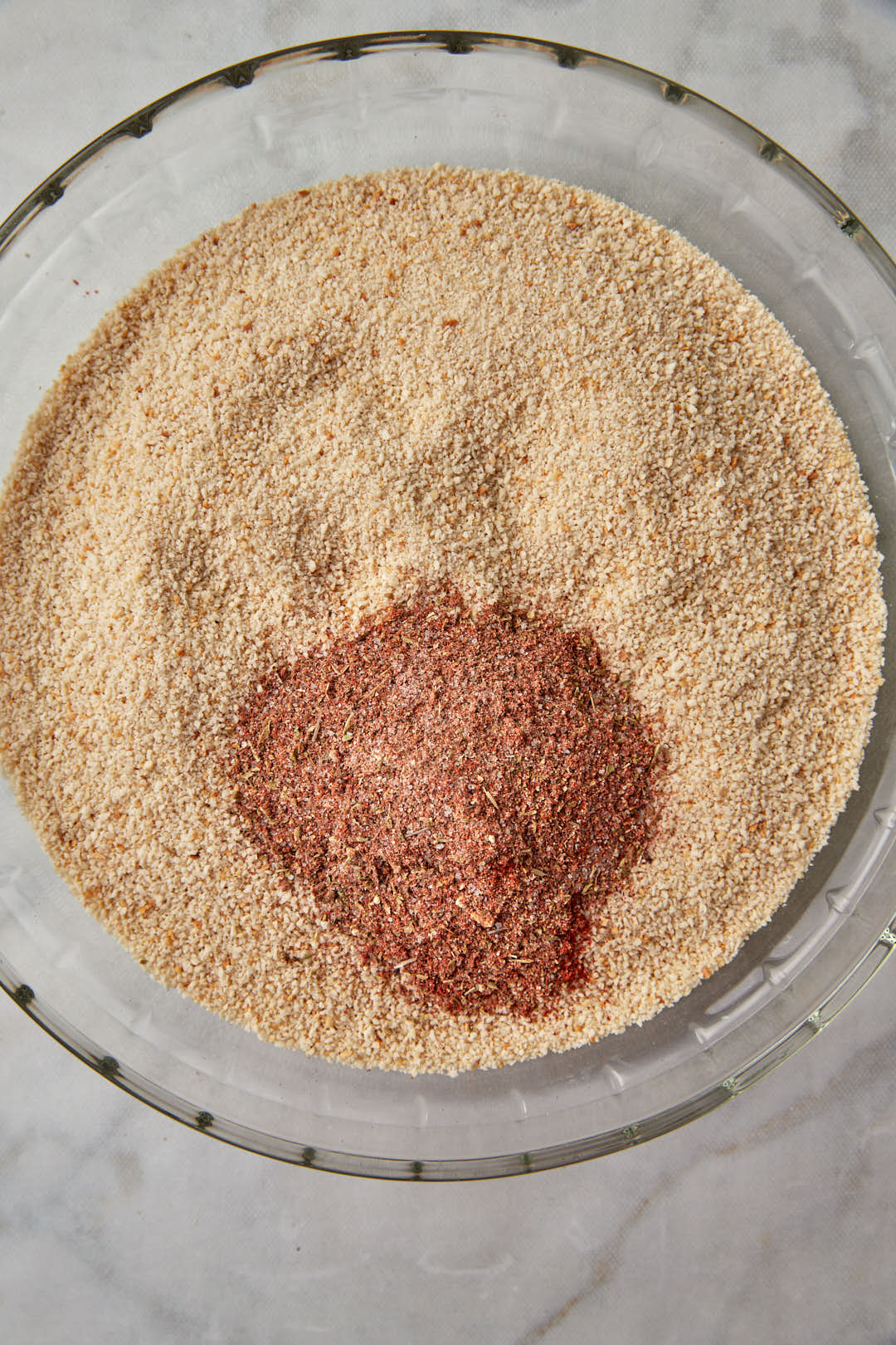 spices added to breadcrumbs in a glass pie plate.