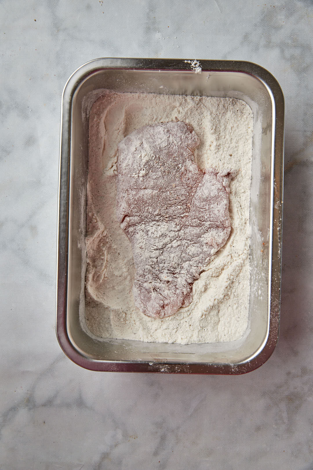 floured chicken breast in container of flour.