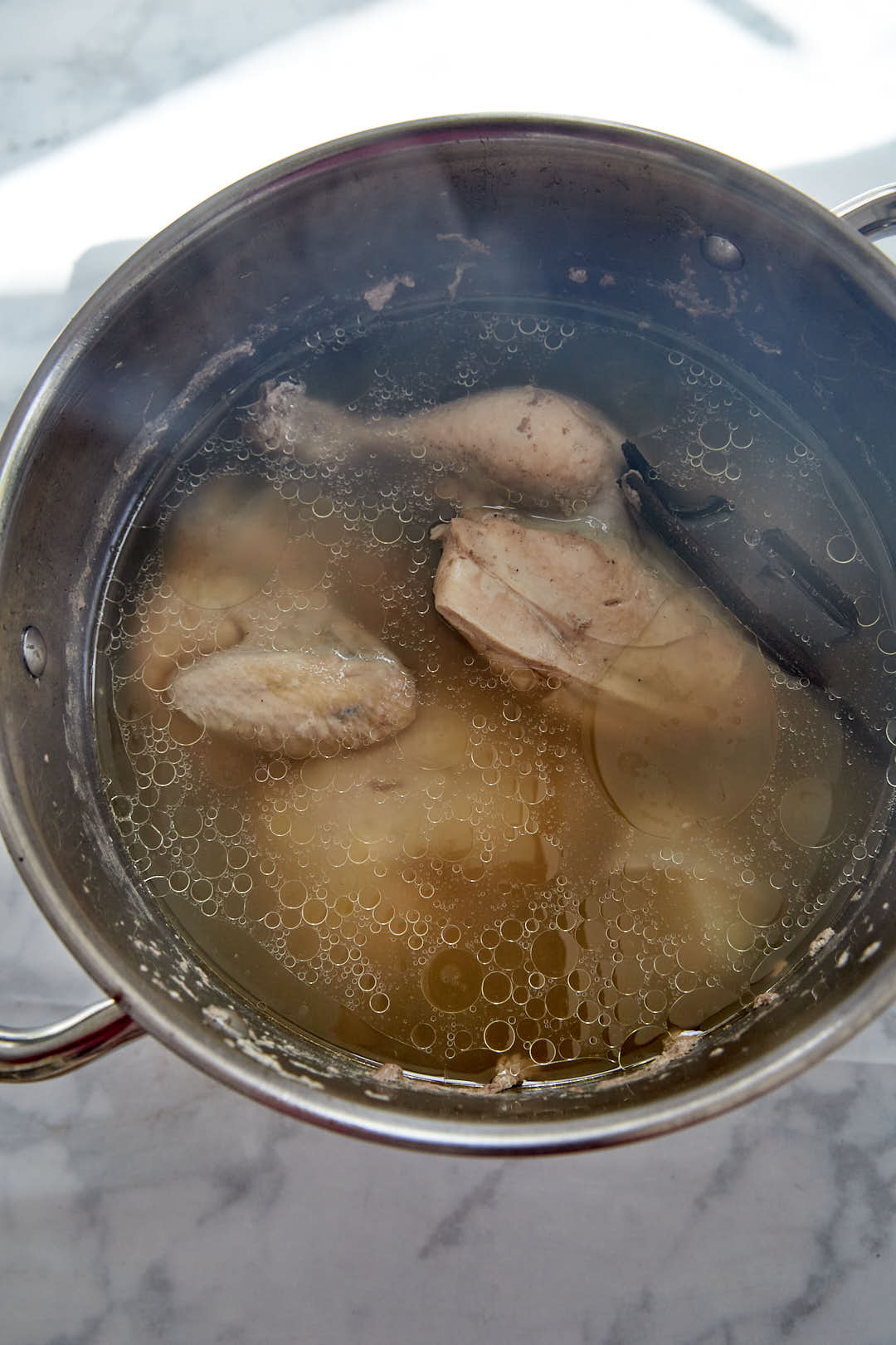 whole chicken being boiled for a chicken stock in a pot.