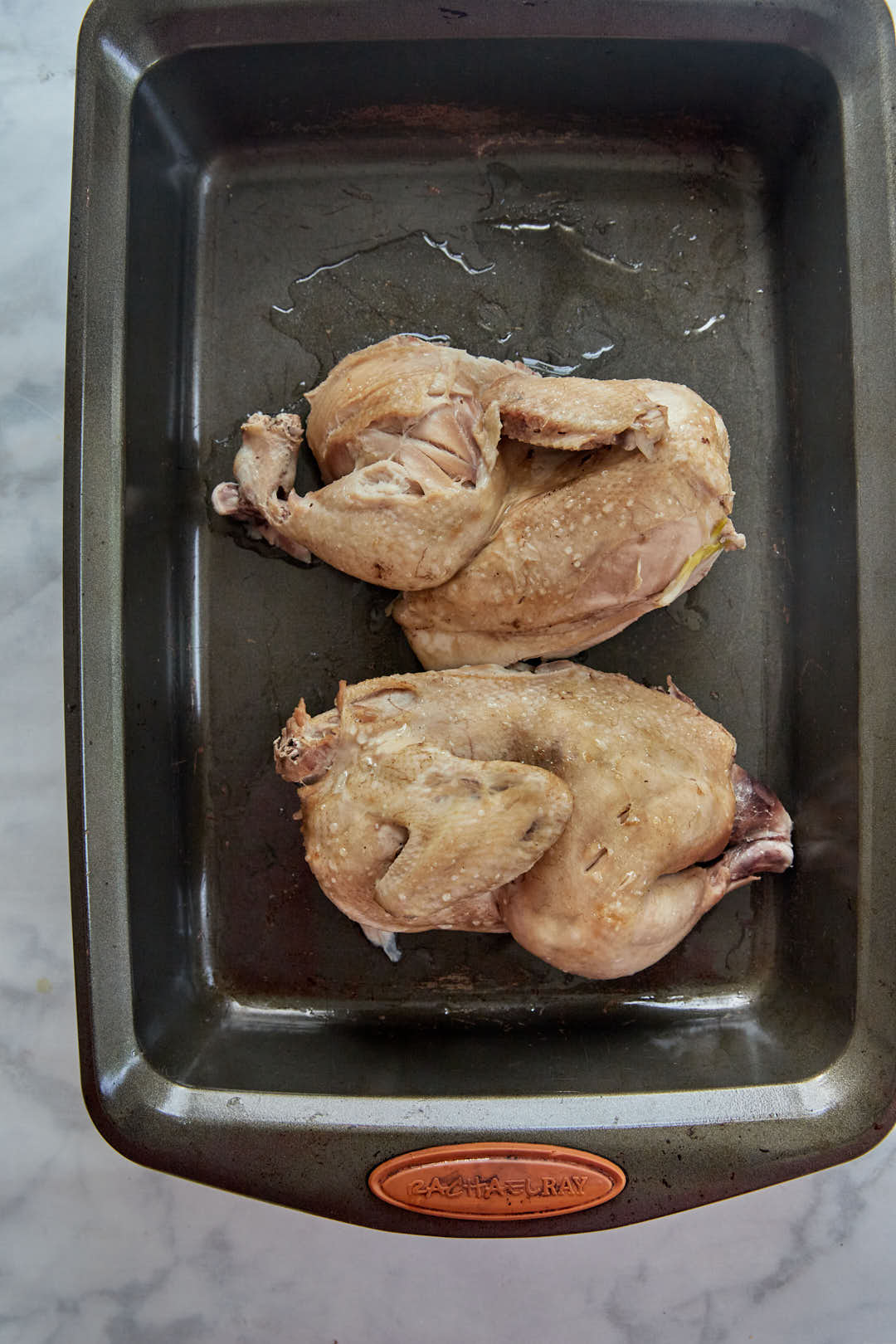 halved chicken on a baking tray before roasting in the oven.