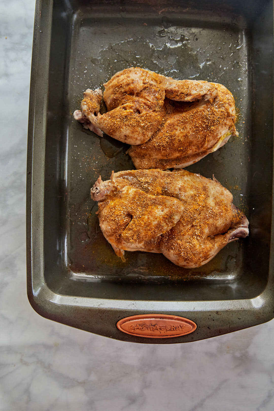 spices rubbed on halved chicken on baking pan.