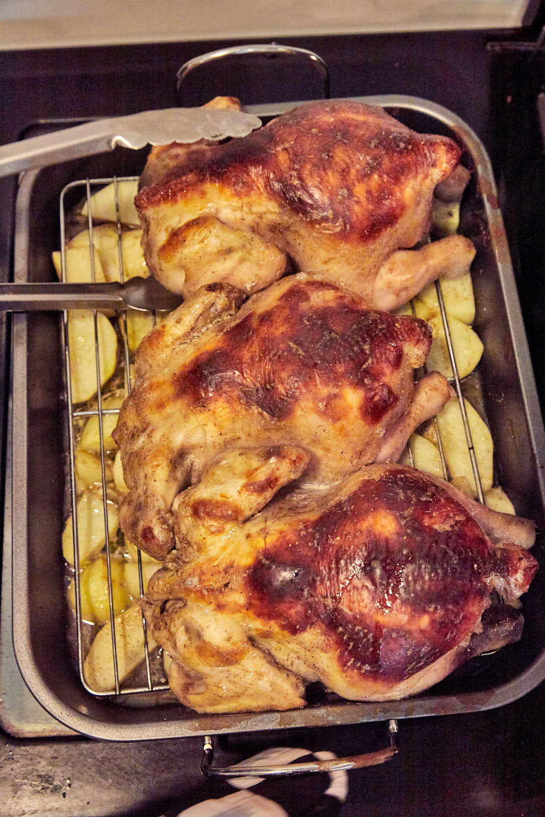 roasted whole chicken son potatoes in a wire rack in a roasting pan.