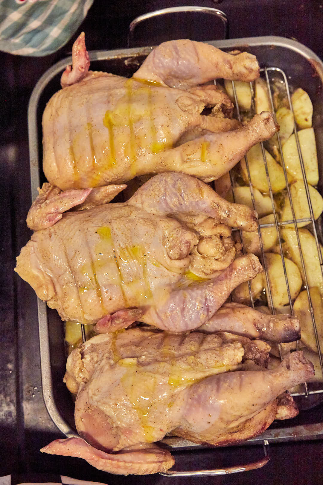 whole chickens on a roasting pan on a wire rack over potatoes.