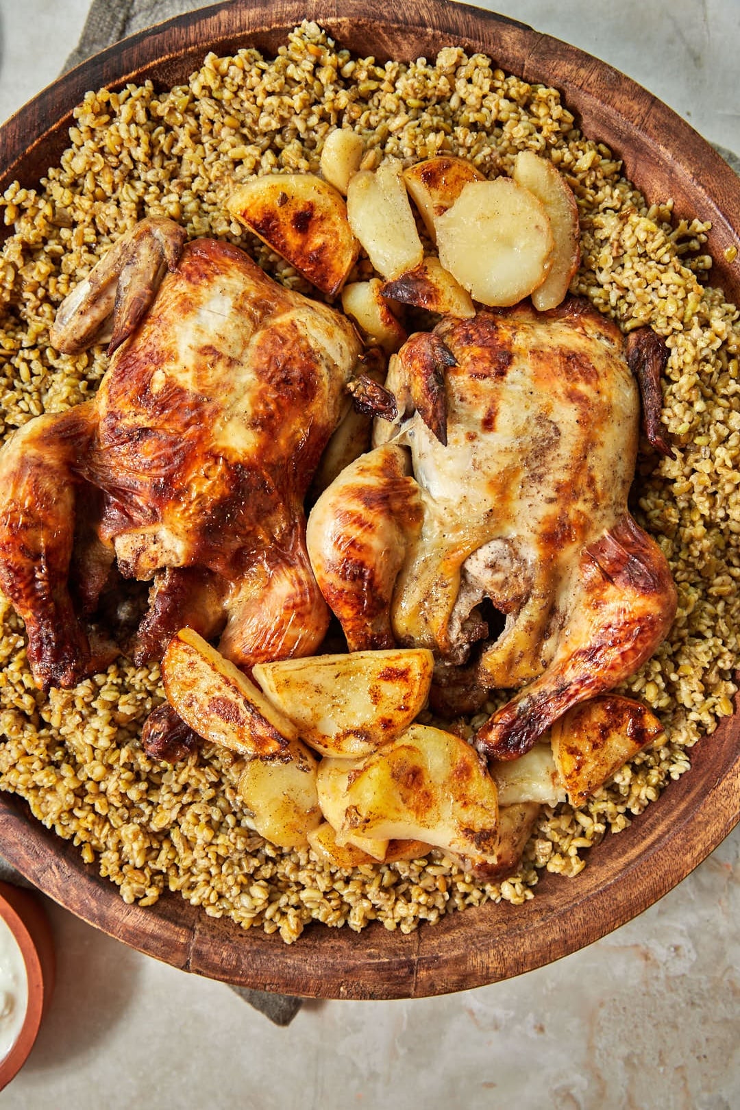 whole roasted chickens and potatoes on freekeh in a large wooden platter.