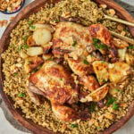 a big wooden platter with freekeh in it plus two whole roasted chickens, potatoes, and toasted nuts.