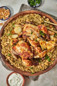 a big wooden platter with freekeh in it plus two whole roasted chickens, potatoes, and toasted nuts.