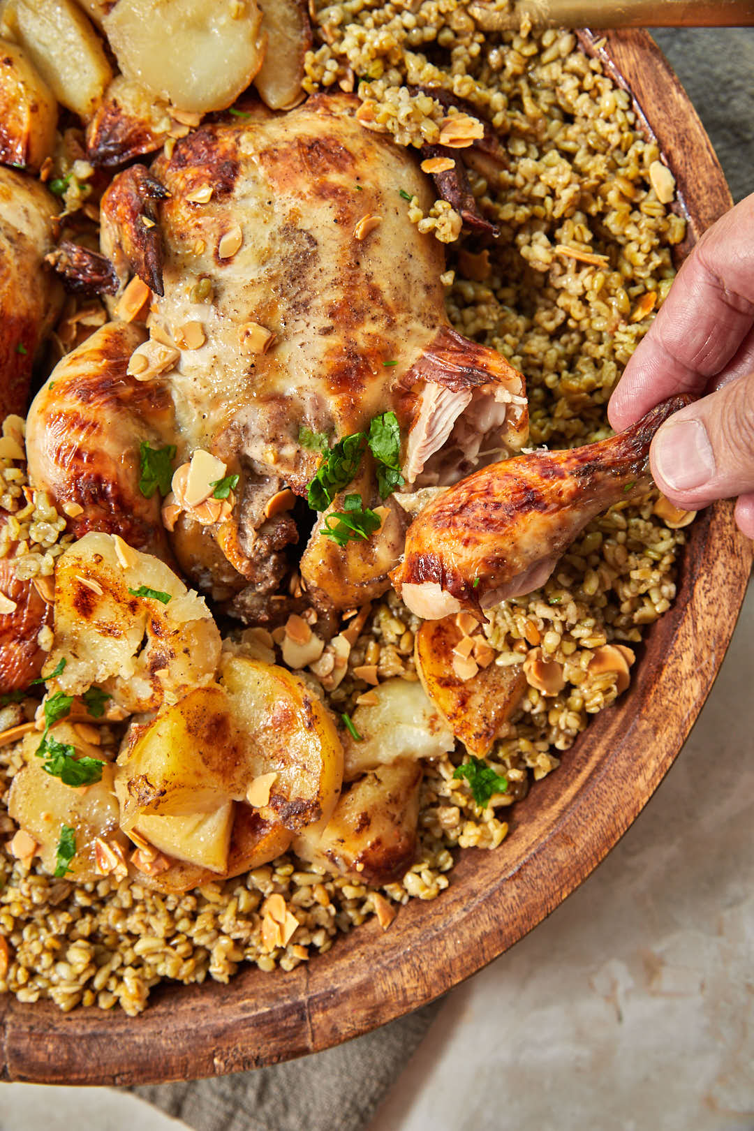 hand holding a chicken drumstick over a platter of freekeh.