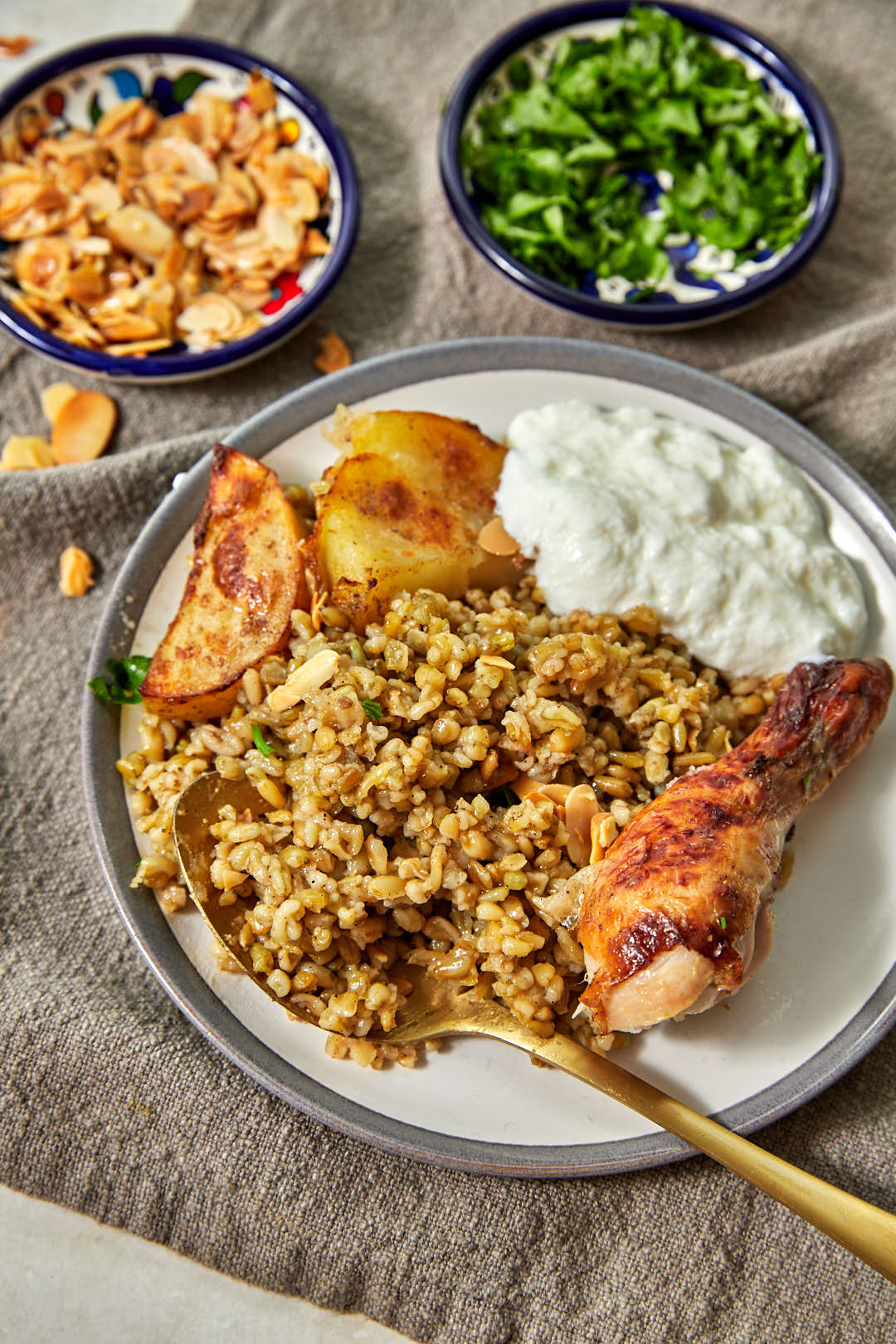 plate of freekeh with a chicken drumstick and potato cubes and yogurt.
