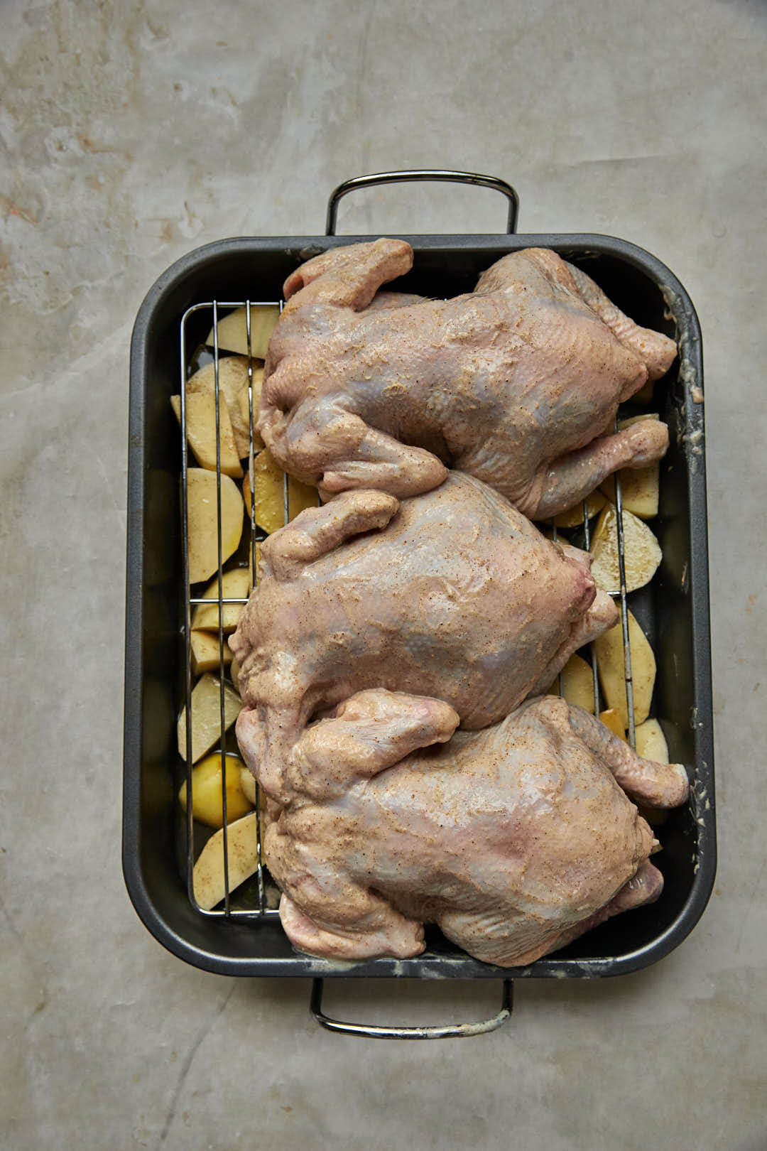 marinated whole chickens on the tray of cubed potatoes in a roasting pan.