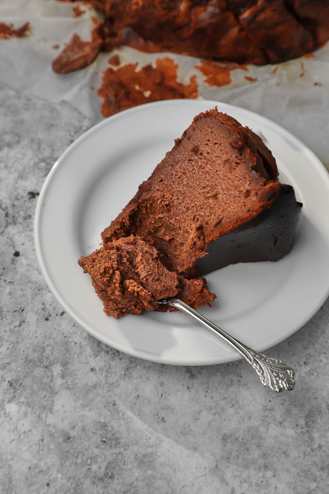 white plate with a slice of chocolate basque cheesecake with a spoon taking a bite out.
