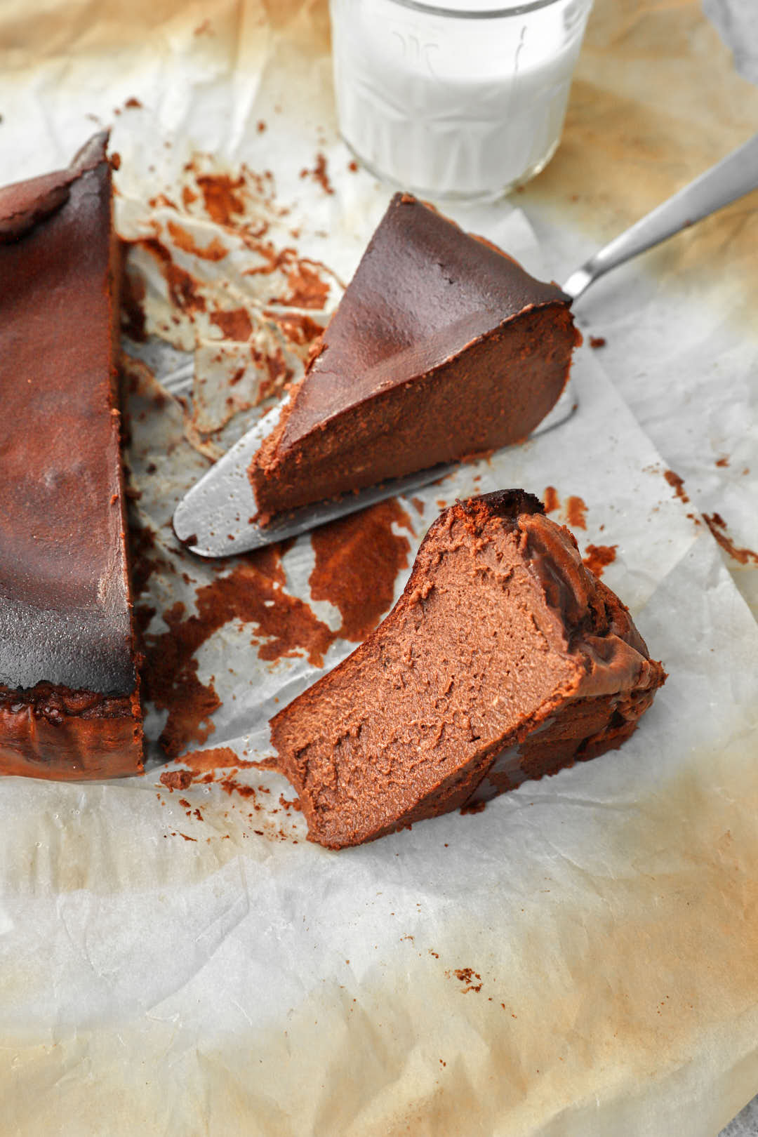 slices of chocolate basque cheesecake on parchment paper with a glass of milk in the background.