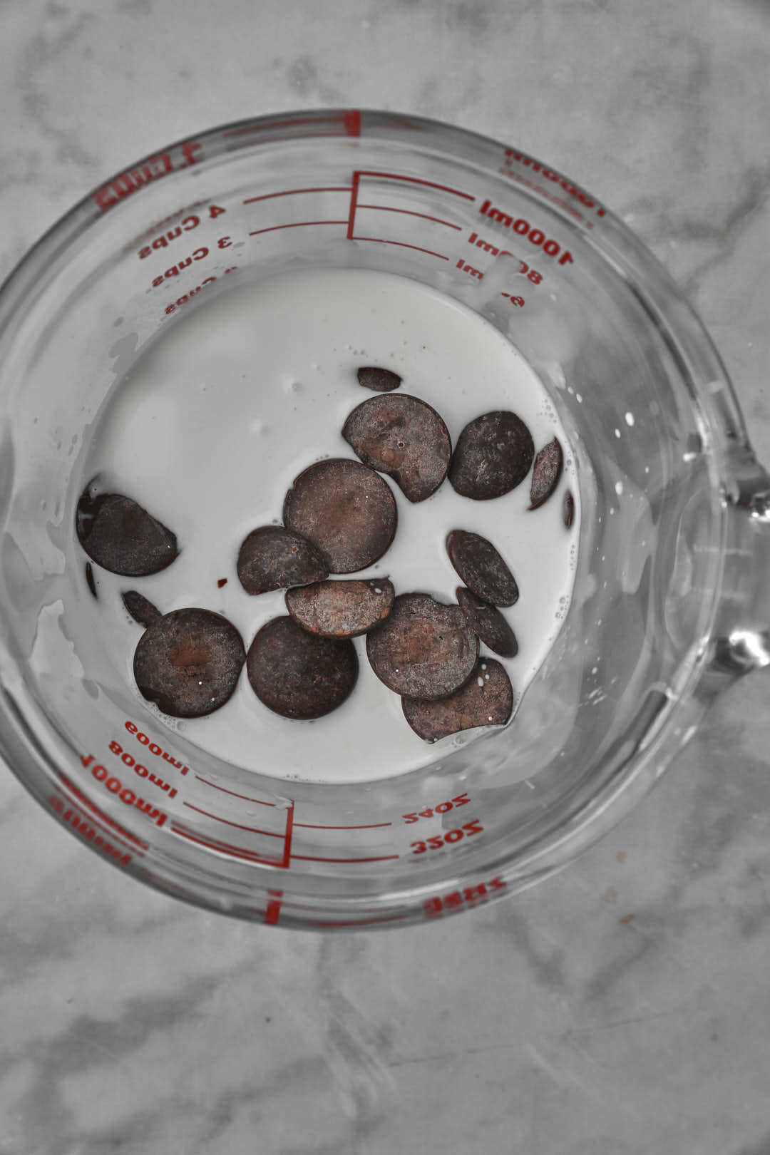 chocolate chunks added to hot heavy cream in a measuring cup.