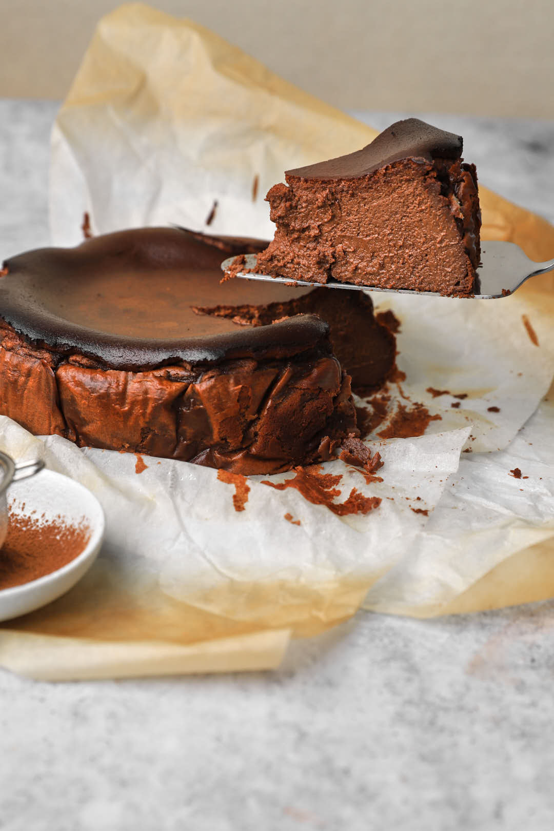 slice of chocolate san sebastian cheesecake lifted in the air with cheesecake in the background.