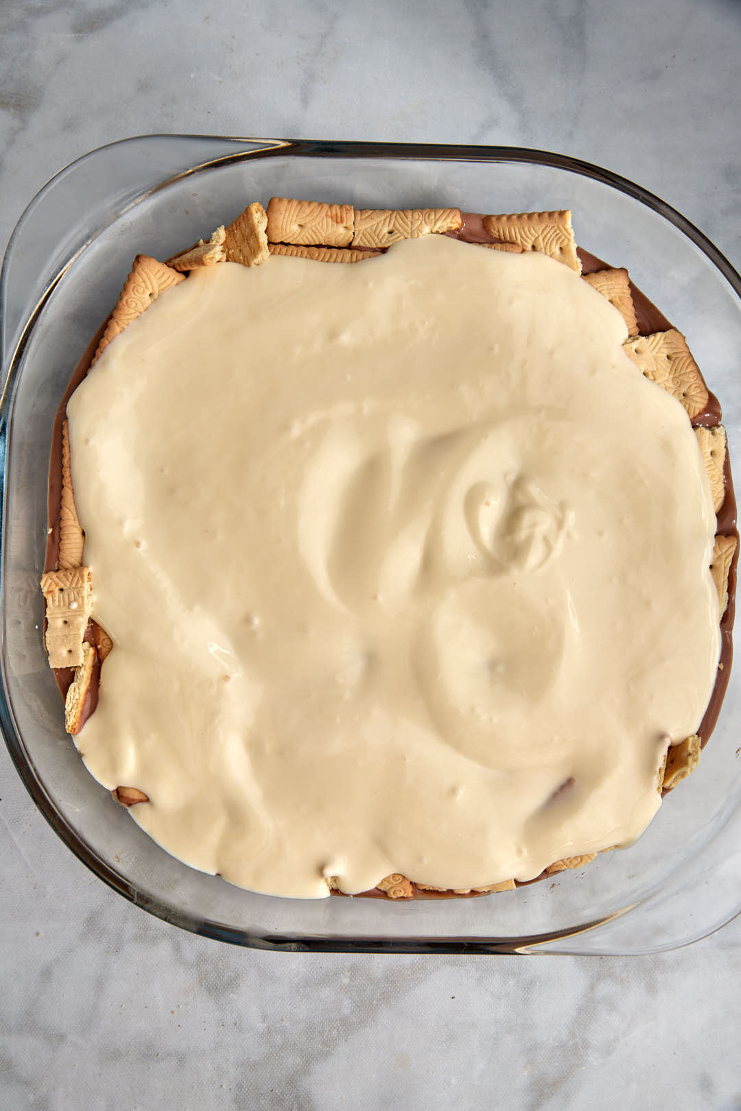 cream spread on a layer of tea biscuits in pyrex pan.
