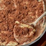 a spoon taking a big scoop of chocolate biscuit pudding out of a pyrex dish.