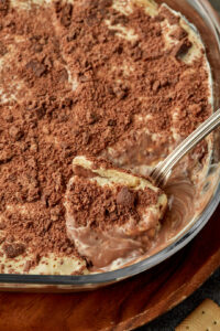 a spoon taking a big scoop of chocolate biscuit pudding out of a pyrex dish.
