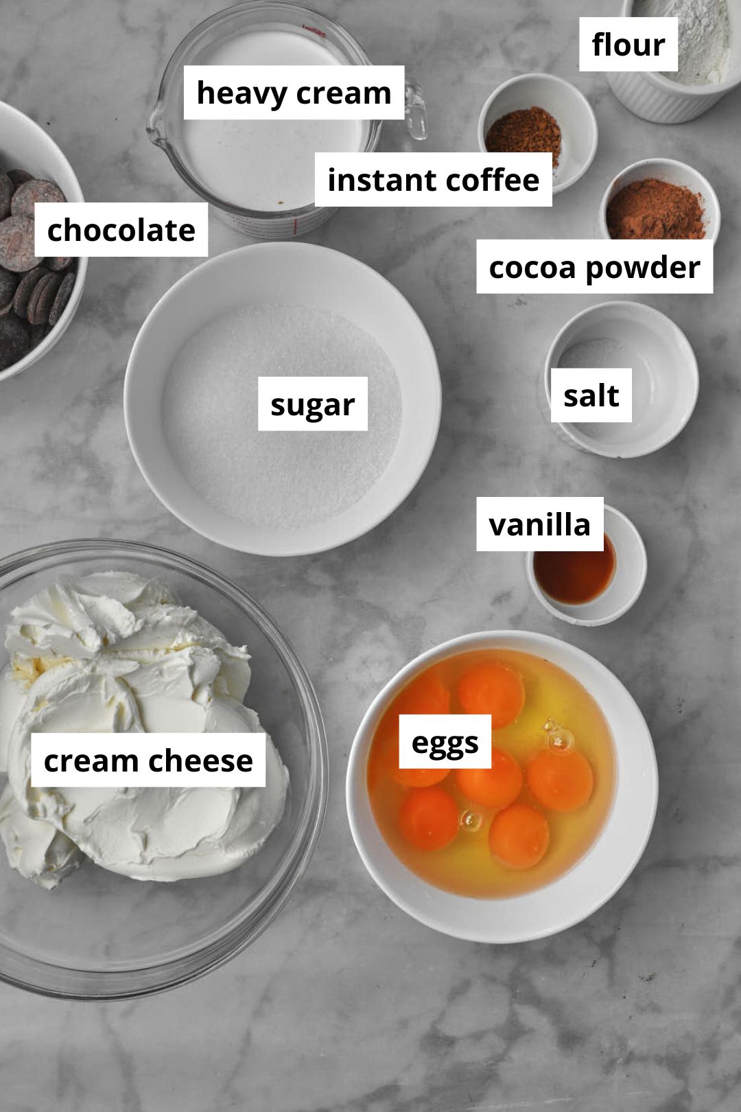 ingredients needed to make chocolate basque cheesecake on a white marble background.
