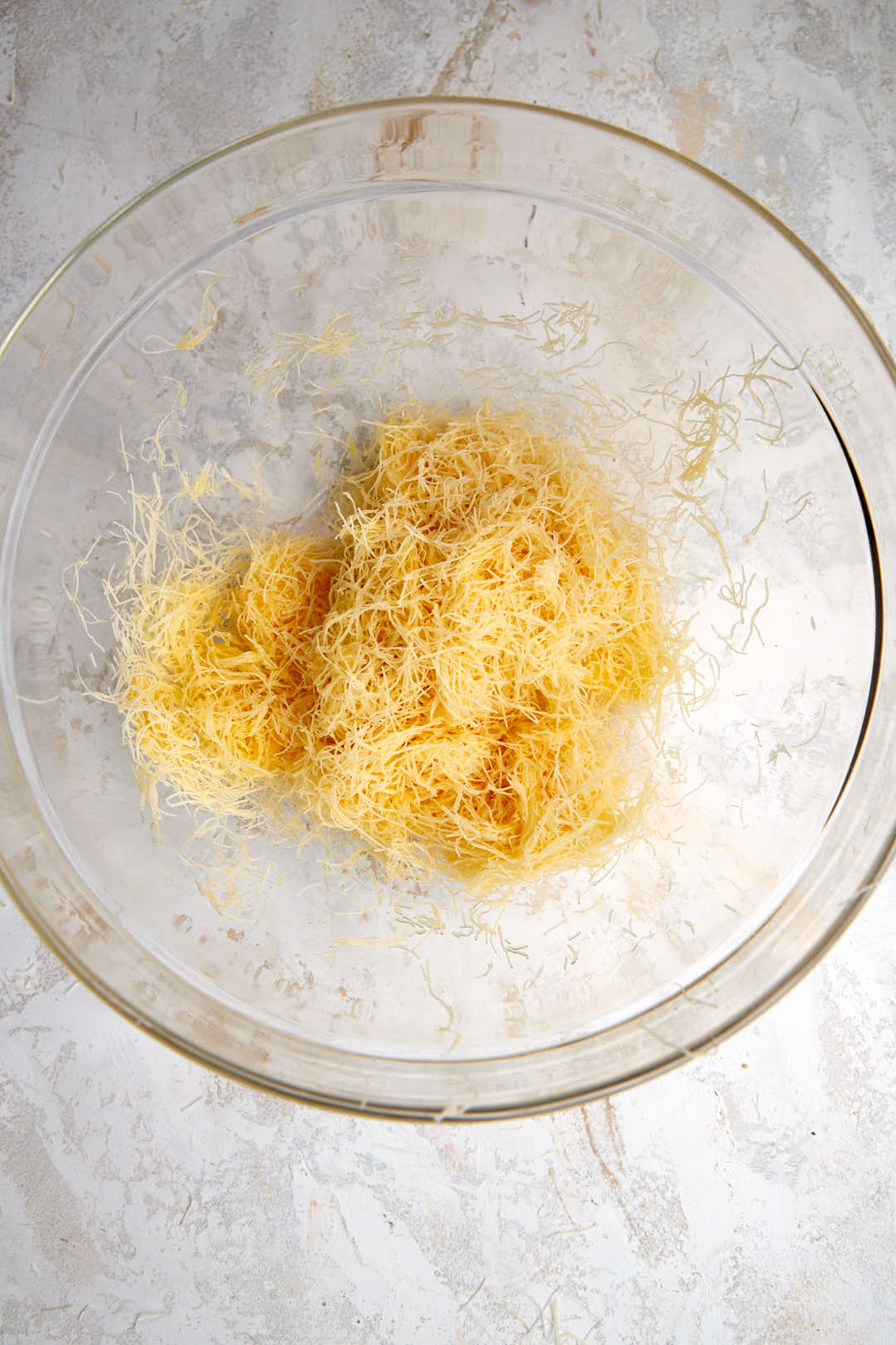 kunafa mixed with melted butter in a glass bowl.