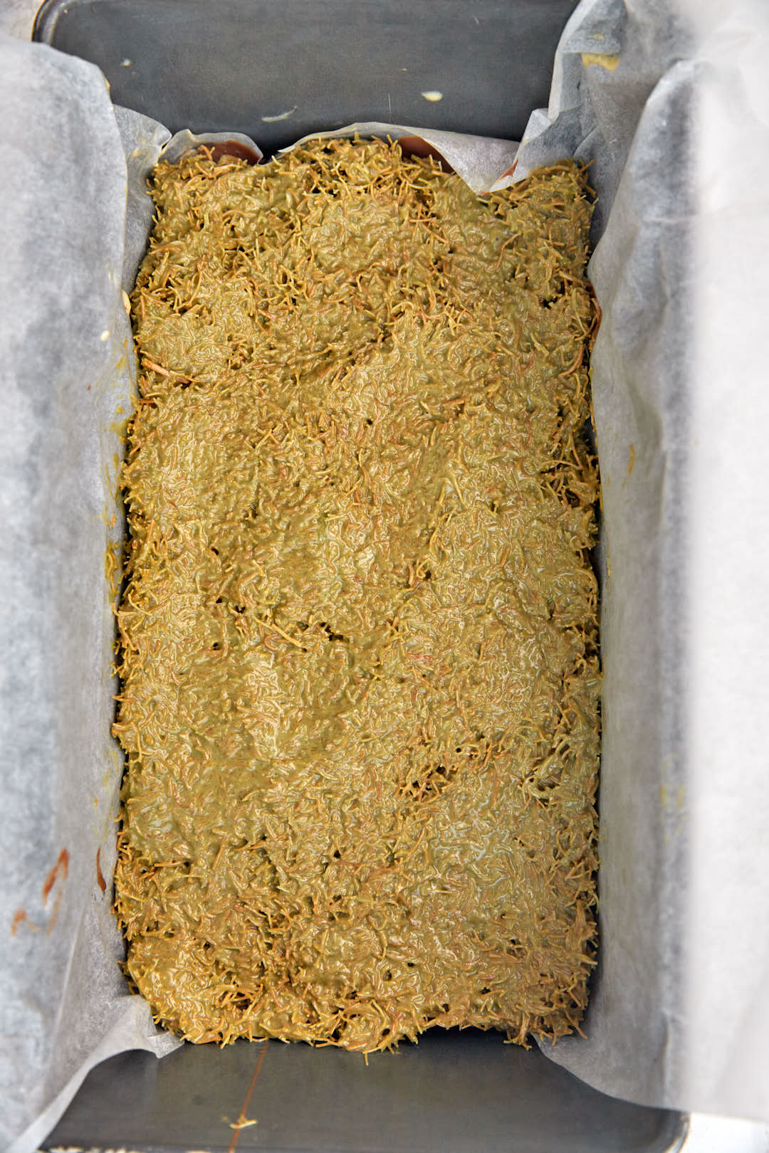 pistachio kunafa filling over chocolate in loaf pan.
