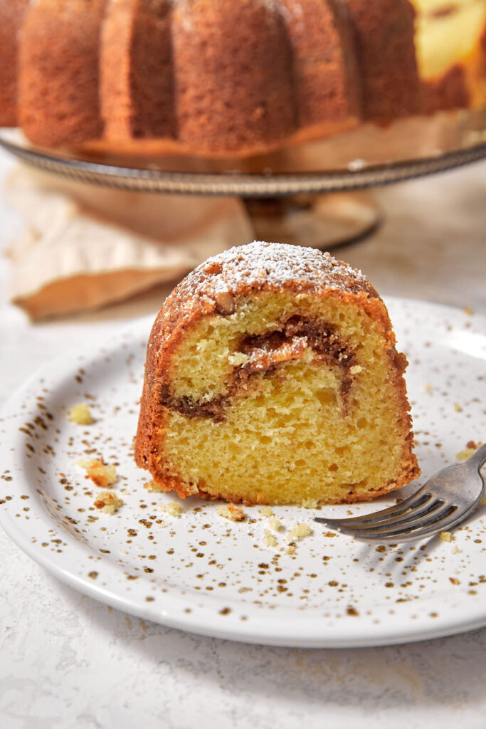 close up photo of a slice of cinnamon bundt cake on a white and brown plate.