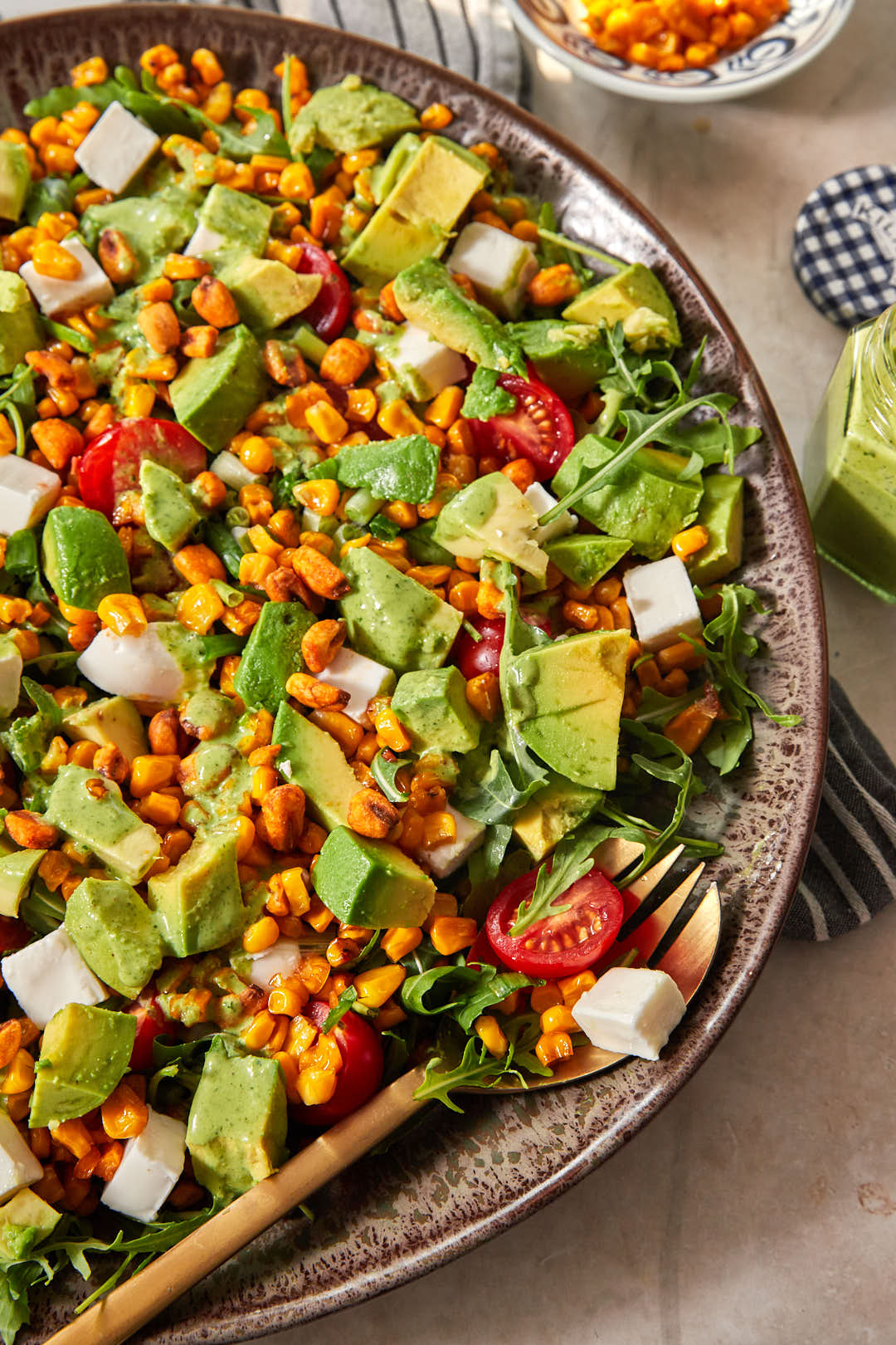 close up photo of a corn avocado arugula salad on a large serving dish.