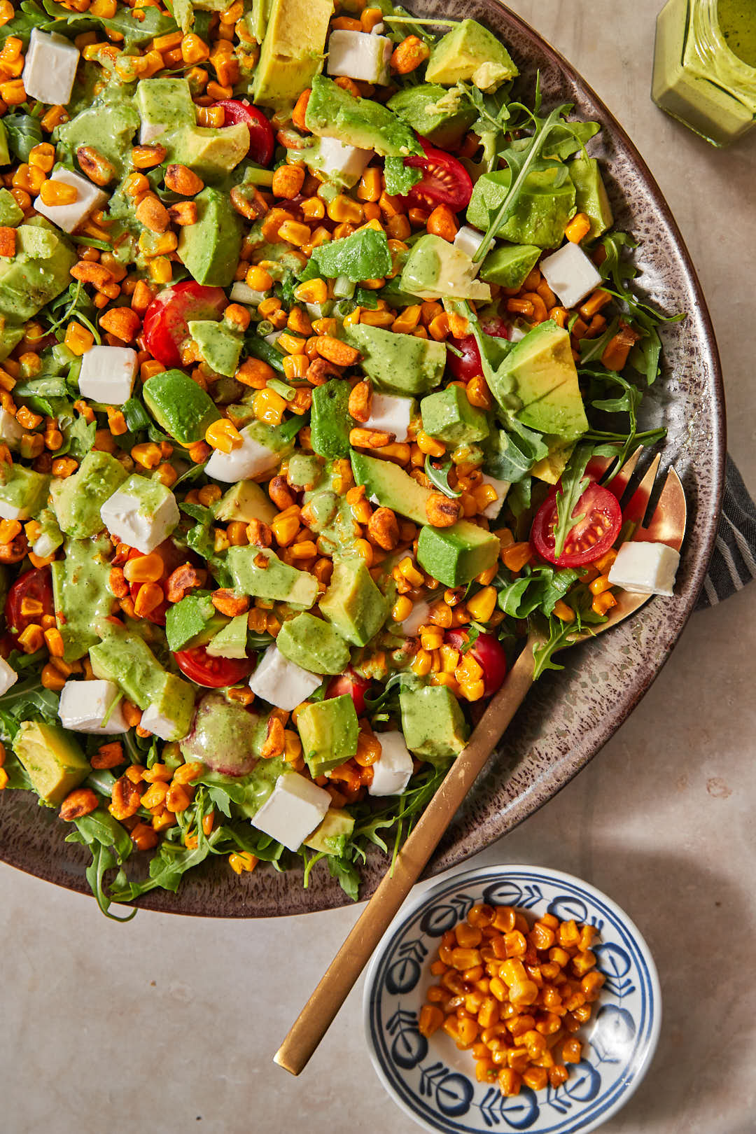 grilled corn, avocado and cherry tomatoes on arugula in a large serving dish, with a small bowl of grilled corn in the background.