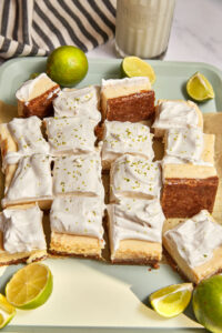 key lime pie bars cut into thick squares and scattered on a mint green tray with extra cut limes in the background.