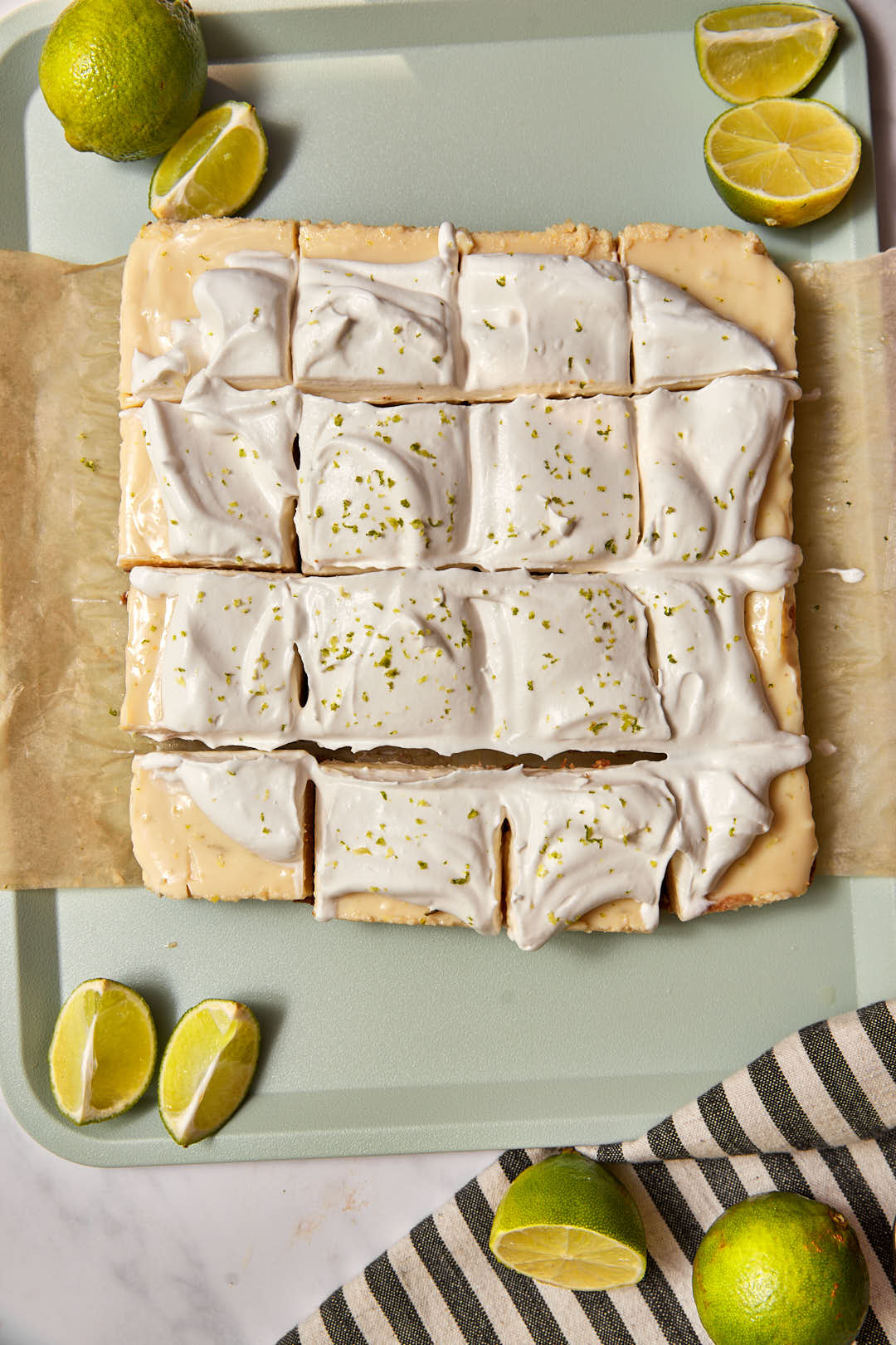 key lime pie bars cut into squares on a mint green tray with extra limes on the side