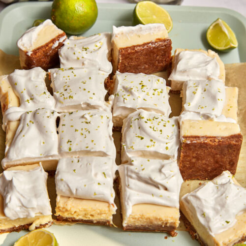 key lime pie bars cut into thick squares and scattered on a mint green tray with extra cut limes in the background.