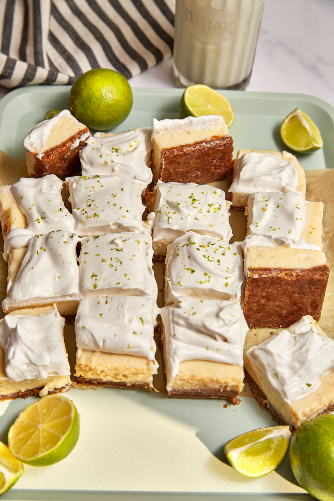 key lime pie bars cut into thick squares and scattered on a mint green tray with extra cut limes in the background.