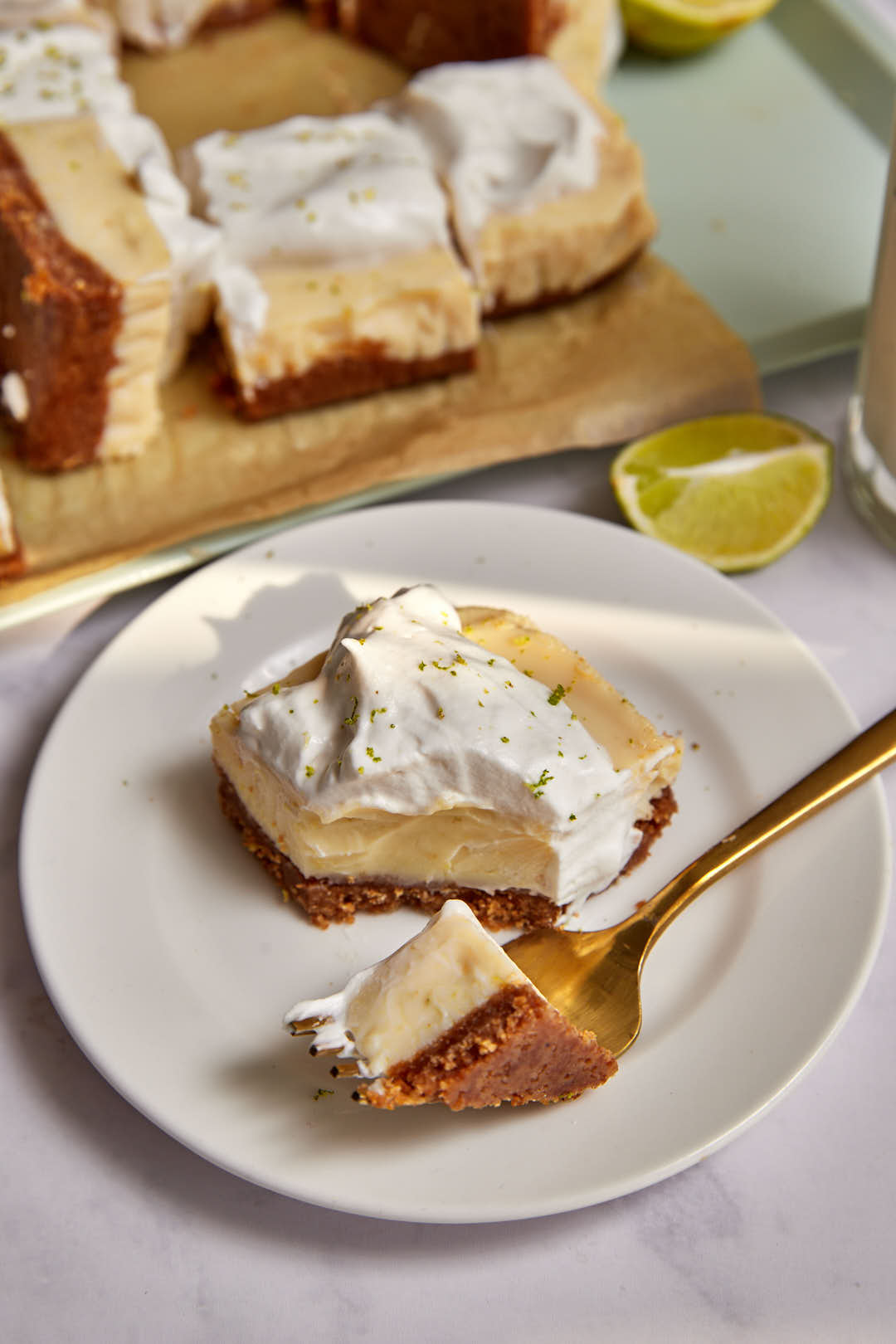 slice of key lime pie on a plate with a small bite being taken out with a golden fork.