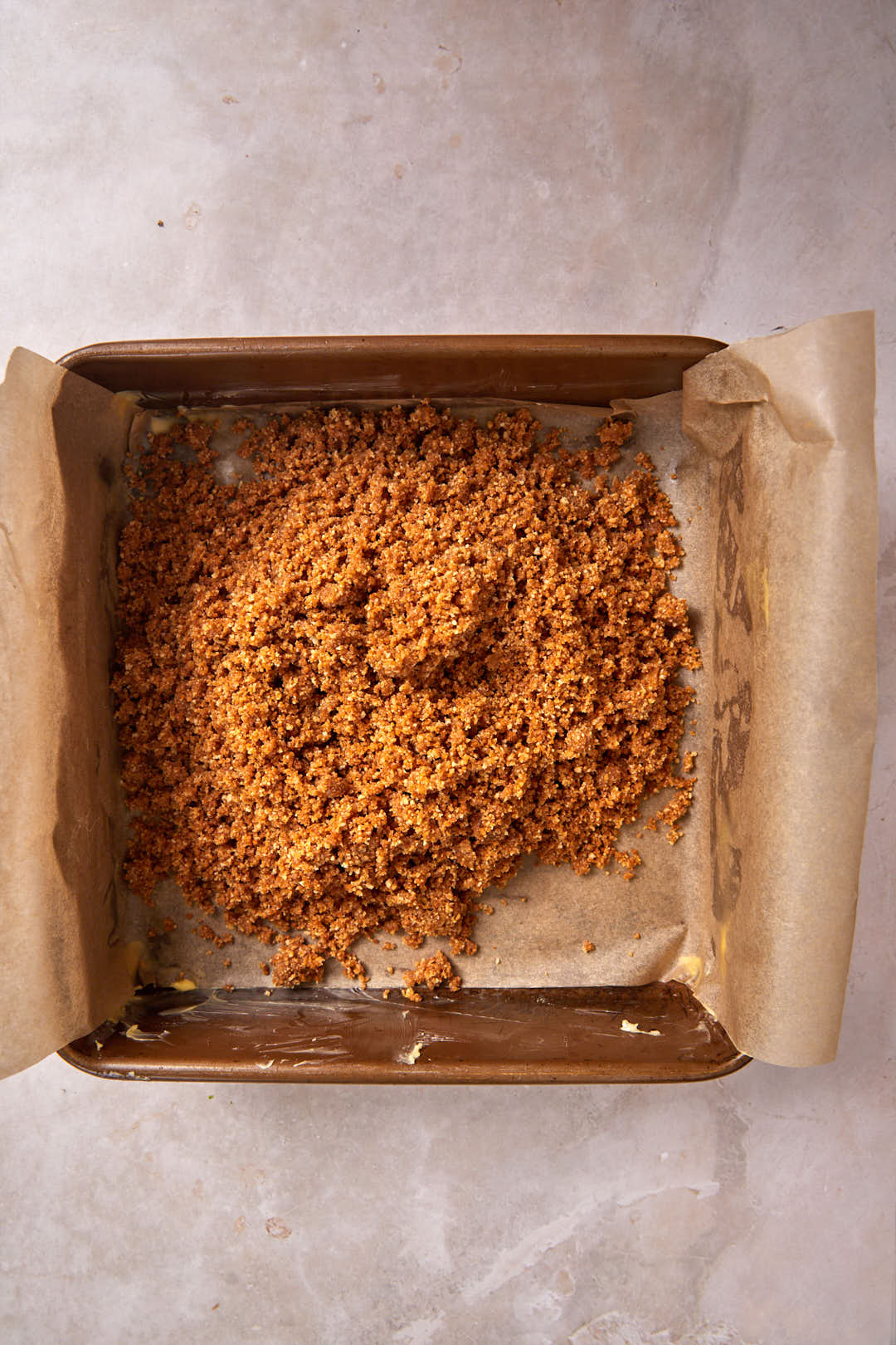 biscoff crust placed in a square baking pan with parchment paper.