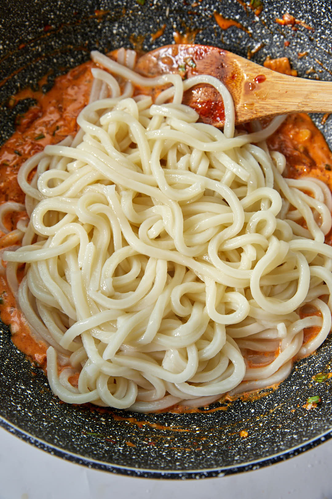 drained udon noodles added to kimchi sauce in a skillet.