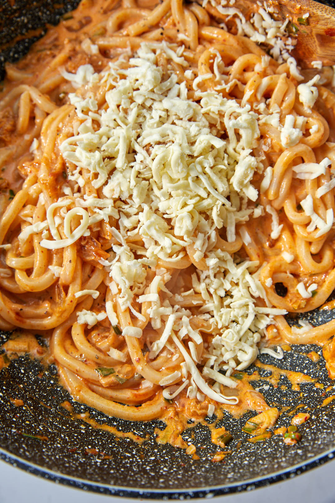 shredded mozzarella cheese added to creamy udon noodles in a large skillet.
