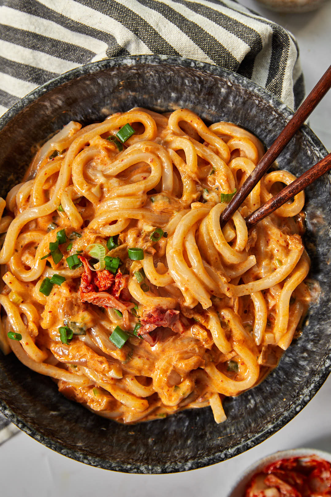 creamy kimchi udon noodles with a chopstick twirling a bite in a black bowl.
