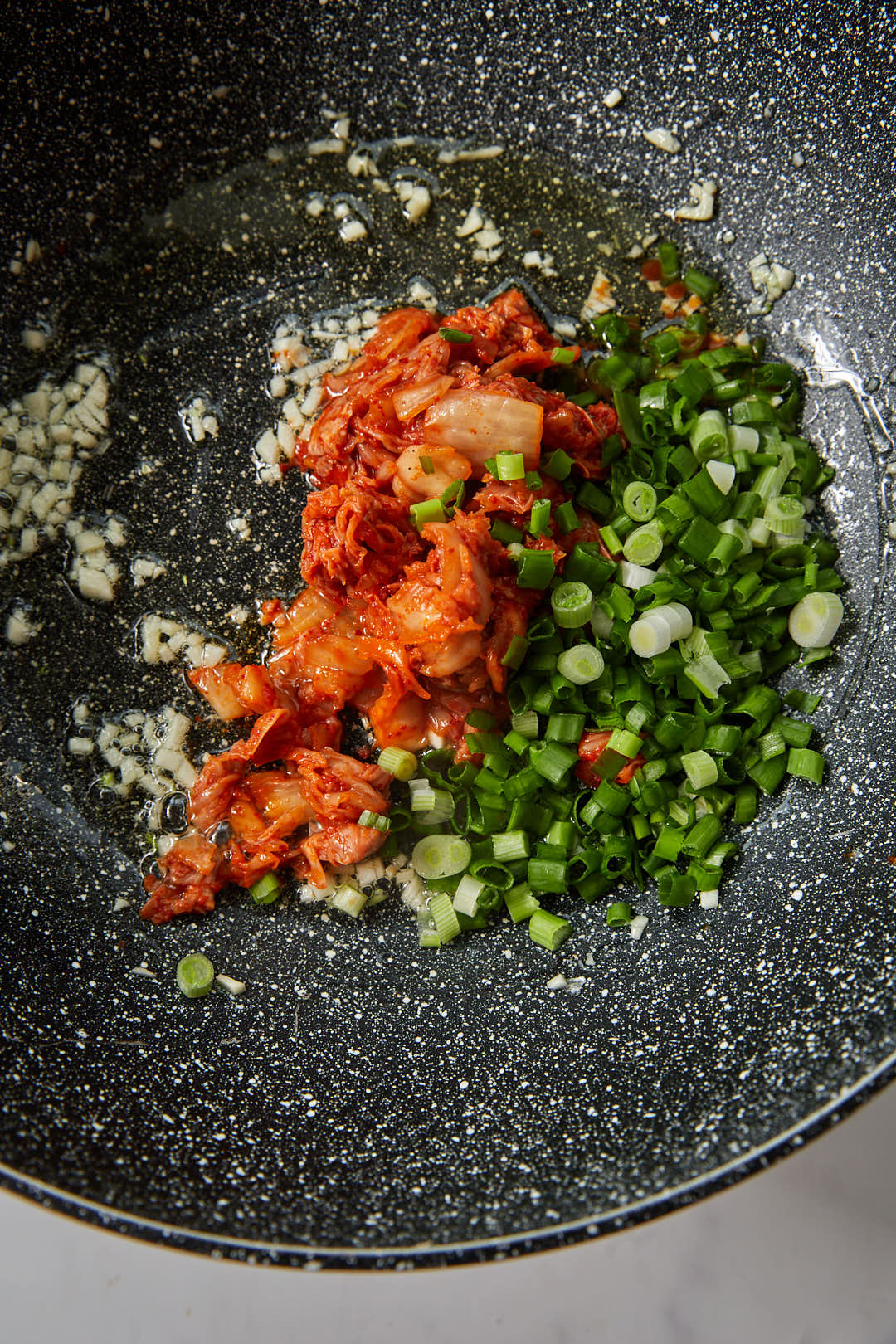 chopped kimchi and sliced green onions added to a large hot sillet.