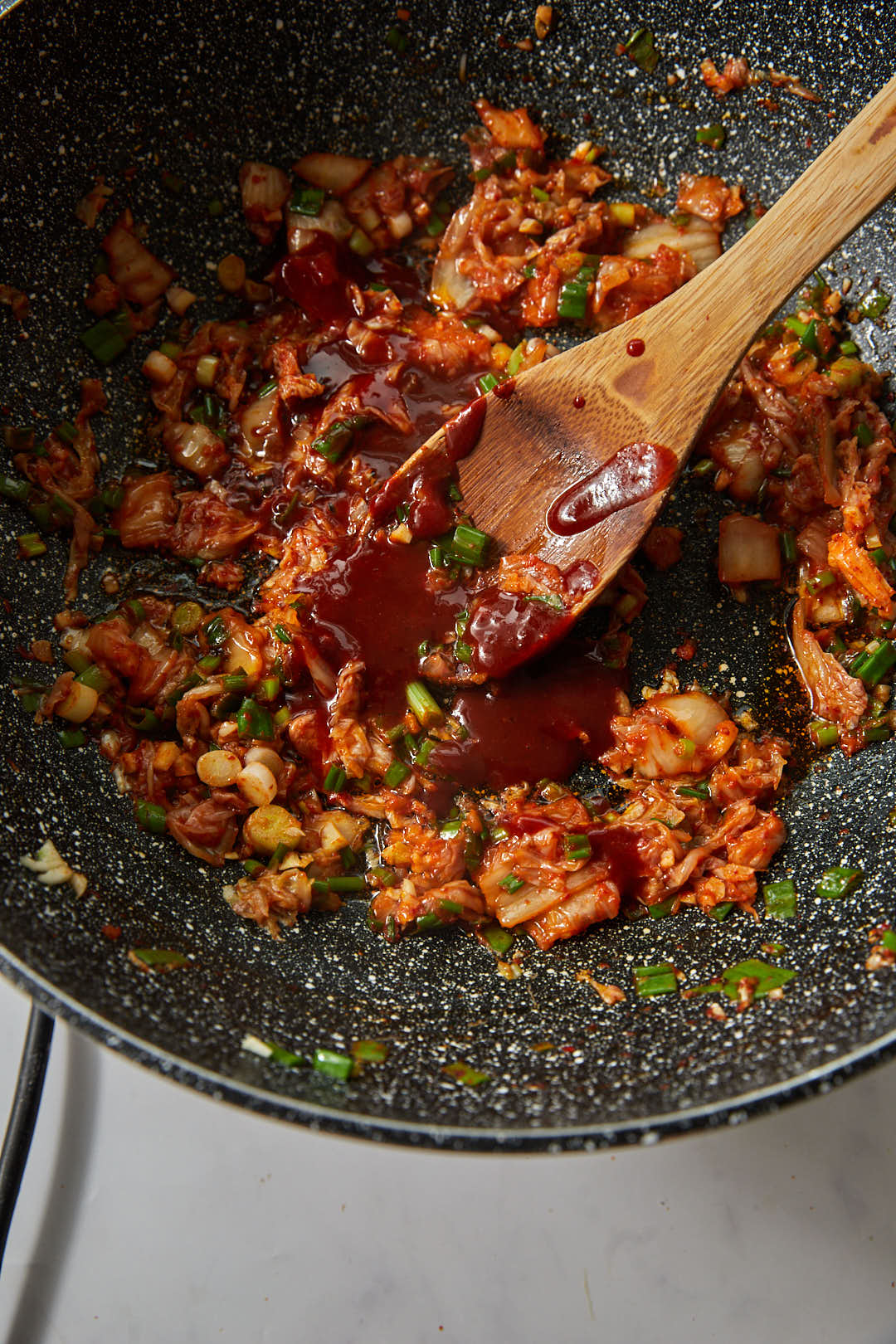 gochujang and chopped kimchi in a large skillet with a wooden spoon.